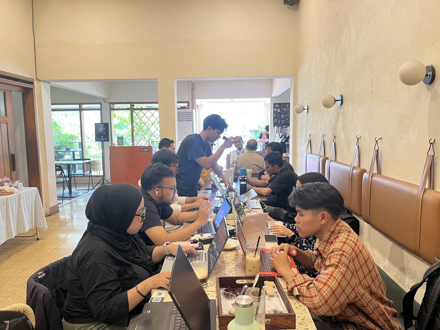Peserta WFC bekerja dengan laptop di meja panjang dalam kafe